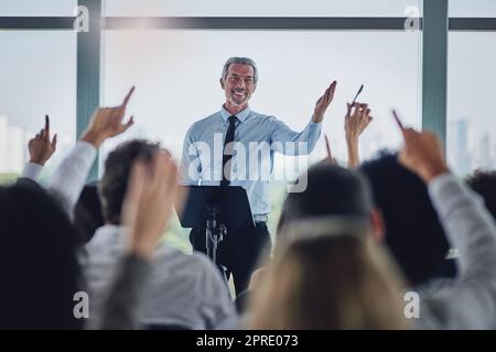 I will answer as many of you as possible. a handsome mature male speaker fielding questions during a seminar in the conference room. Stock Photo