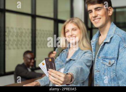 Cheerful young couple check in at hotel reception counter, female holding two credit card. Stock Photo