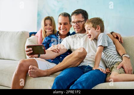 Family fun. an affectionate family of four taking selfies on the sofa at home. Stock Photo