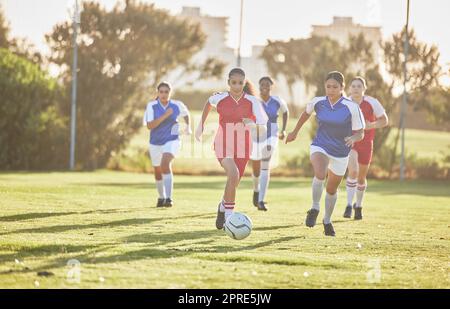 Female football, sports and team playing match on a field while passing, touching and running with a ball. Active, fast and skilled soccer players in a competitive game on a pitch outdoors. Stock Photo