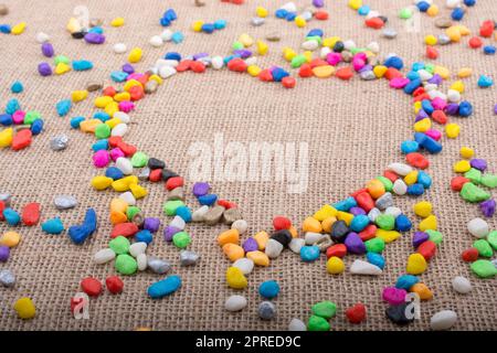 Colorful little pebbles form a heart shape on canvas ground Stock Photo