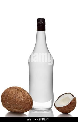 Bottle of alcohol beverage with coconut flavour with whole and opened coconuts with reflection on white background. Stock Photo