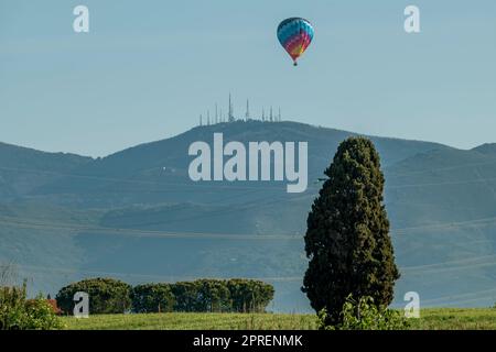A colorful hot air balloon flies over the Tuscan countryside with Monte Serra in the background, Pisa, Italy Stock Photo