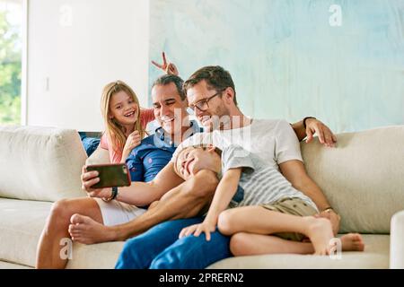 Taking silly selfies on the sofa. an affectionate family of four taking selfies on the sofa at home. Stock Photo
