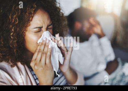 Ill or sick woman with allergy, sinus infection sneezing in tissue or blowing nose during flu season at home. Sick girl caught a bad cold showing symptoms of covid, or suffering from a virus disease Stock Photo