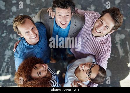 Cheerful, united and diverse group of young business colleagues in collaboration for corporate trust building. Top view of coworkers looking up, smiling and standing close together. Stock Photo