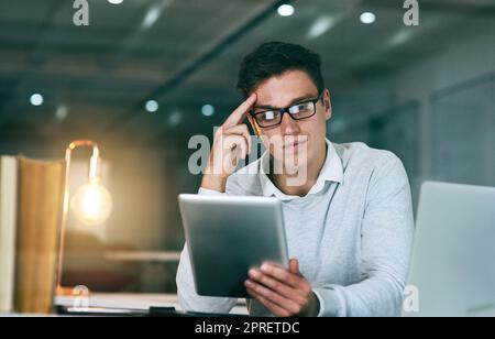 This challenge will require a bit of deep thinking. a handsome young businessman using a digital tablet in an office at night. Stock Photo