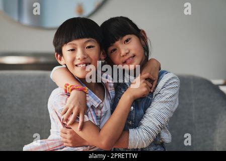 Brother and sister love. Portrait of a cheerful brother and sister holding each other while being seated on a couch at home during the day. Stock Photo