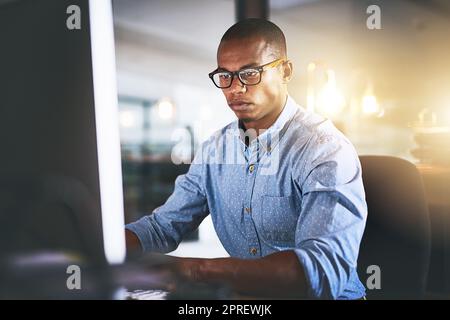 Success follows the focused. a young businessman using a computer during a late night in a modern office. Stock Photo