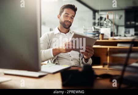 Staying updated with it all. a handsome young businessman using a digital tablet while working late in an office. Stock Photo