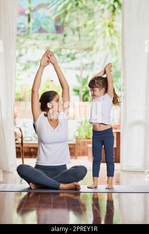 Stretch up high as far as possible. a focused young mother and daughter doing a yoga pose together with their arms raised above their heads. Stock Photo