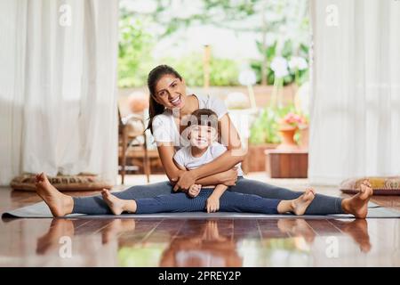 Nothing like the bond between a mother and daughter. Portrait of a cheerful young mother and daughter doing a yoga pose together while holding each other in a spit position. Stock Photo