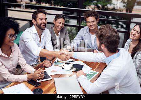 Lets take over the business world. two handsome young businessmen shaking hands while sitting with their colleagues outdoors. Stock Photo