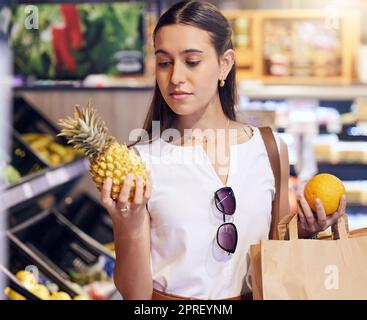 Shopping, holding and looking at fruit at shop, buying healthy food and examining items at a grocery store. Woman deciding, choosing and picking ripe, fresh and delicious produce alone at a market Stock Photo