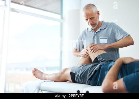 Were going to take recovery one step at a time. a handsome mature male physiotherapist treating an unrecognizable patient. Stock Photo