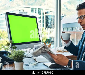 Starting off his day with coffee and the newspaper. a focused young businessman seated at his desk while drinking coffee and reading a newspaper in the office. Stock Photo