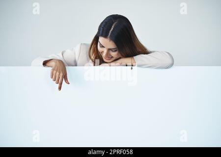 If you could direct your attention over here... Studio shot of an attractive young businesswoman pointing at copy space on a blank placard. Stock Photo