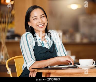 Coffee shop owner looking proud and happy while doing paperwork and having coffee break. Young business woman checking stock, orders and inventory, enjoying her career. Positive lady managing a cafe Stock Photo