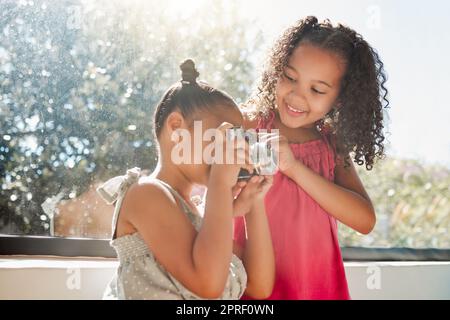 Cute sisters bonding, taking photos on camera at home, smiling while being playful and curious. Little girls playing, having fun together, enjoying their bond and sharing precious childhood moments Stock Photo