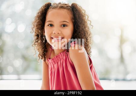 Cute, adorable and sweet young girl with a happy and healthy childhood growing up at home. Portrait of an innocent young female child with a bright smile and relaxing in the house Stock Photo