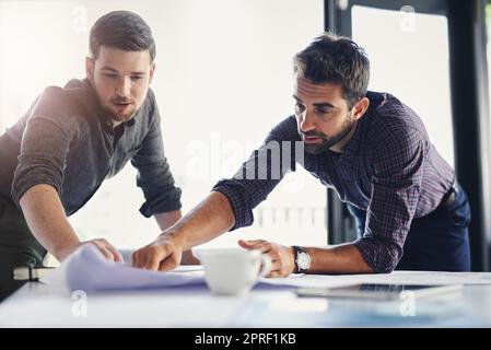 Lets go through the work one more time. two young businessmen working through business plans together inside of the office. Stock Photo