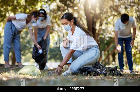 Group of volunteers picking up, cleaning and reducing pollution in a public nature park together. Diverse community wearing face masks to protect from disease, collecting dirt and doing cleanup Stock Photo