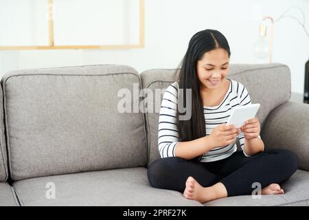 Who said learning stops after you come home from school. a happy young girl relaxing on the sofa and using a digital tablet. Stock Photo