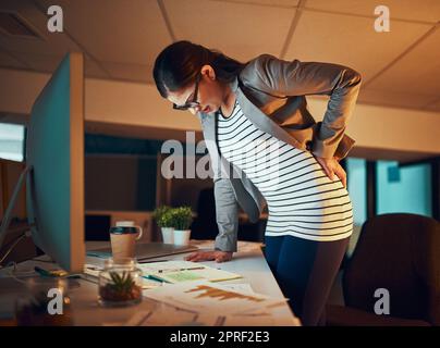 Sitting all day is giving her back problems. a young businesswoman experiencing body discomfort in the office. Stock Photo