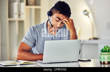 Stressed, tired and frustrated call center agent feeling sick or ill in the office while working on his laptop. A worried and unhappy young telemarketing employee suffering from a headache and pain Stock Photo