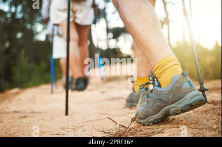 . Feet or shoes walking, trekking and hiking on a trail up a mountain with sticks and poles. Closeup of group of adventurous hikers or friends exploring rugged path on a mountain in nature. Stock Photo