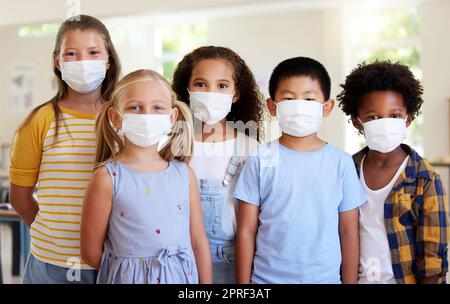 School kids, education and covid while wearing face masks in a classroom for protection against covid. Portrait of cute, young and smart students in safe learning and educational environment together Stock Photo
