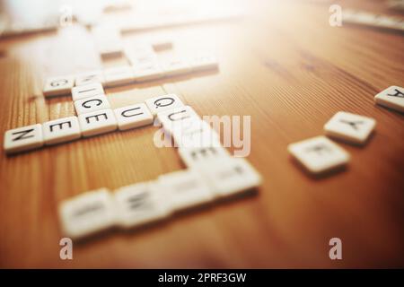 Scrabble, board games and fun with pieces on a table making words, text and language while playing a game. Spelling, entertainment and recreation with a word association activity in a house or home Stock Photo