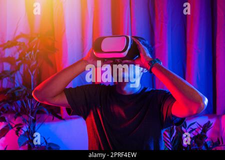 Asian handsome man wear VR helmet excited emotional at home purple and blue background Stock Photo