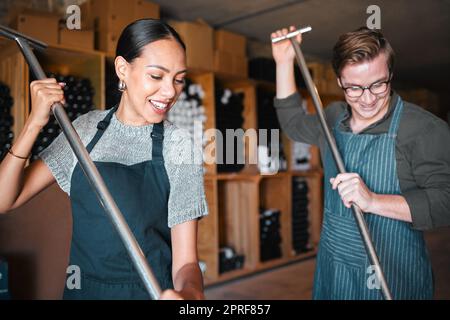 Winemaker workers in wine production using press tool for mixing or pressing in a warehouse, winery or distillery. Teamwork people, woman and man working on quality alcohol, manual labor in a cellar Stock Photo