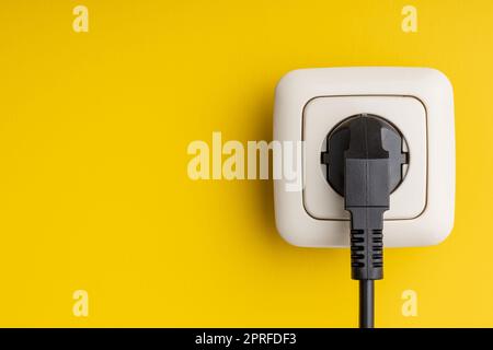 Electric plug and wall socket on yellow wall. Stock Photo