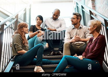 Chatting about business. a group of businesspeople sitting together on a stairwell. Stock Photo