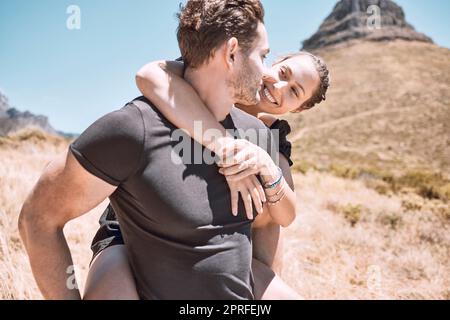 Piggyback, happy and in love couple having fun, being active and enjoying quality time together outdoors. Cute, sweet and loving boyfriend and girlfriend bonding on an adventurous and cheerful date Stock Photo