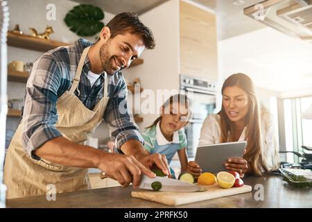 There are so many exciting recipes to try online. two happy parents and their young daughter trying a new recipe in the kitchen together. Stock Photo