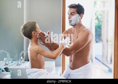 Your turn. a handsome young man teaching his son how to shave in the bathroom. Stock Photo