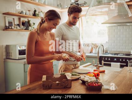 Cooking food, happy and healthy couple preparing a dinner meal in the kitchen together at home. Excited, carefree and joyful lovers doing smiling and laughing while making food or lunch Stock Photo
