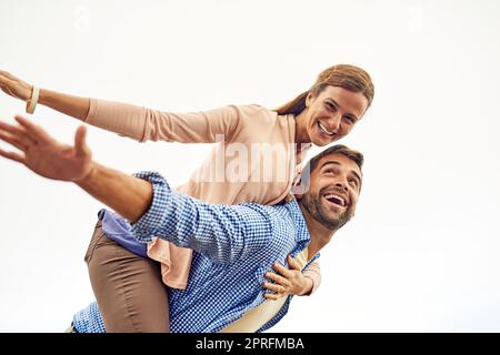 Being in love is the best feeling ever. a man piggybacking his girlfriend while spending the day outdoors. Stock Photo