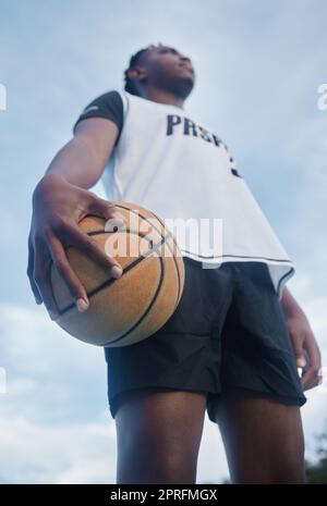 Basketball athlete ready for training, game and competition on sports court from below outdoor. Thinking, focus and fitness young black man with motivation, mindset and goal to play, win and have fun Stock Photo