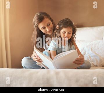 Once upon a time. a happy mother and daughter at home reading a storybook on the bed. Stock Photo