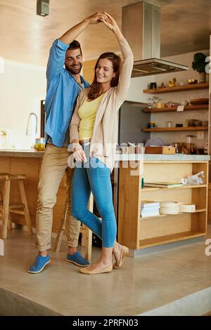 Dancing joyfully. Full length shot of an affectionate young couple dancing in their kitchen. Stock Photo