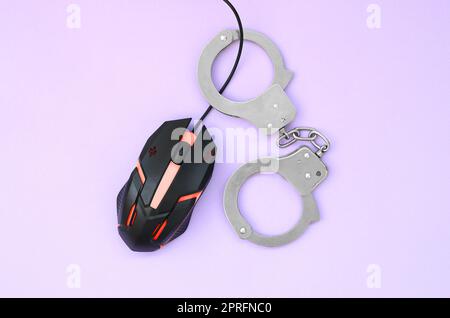 Computer mouse in a red color is chained in handcuffs on the background of purple color. The concept of combating computer crime, hackers and piracy. Stock Photo