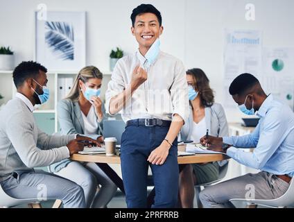 Meeting, partnership or collaboration by business people during covid in an office planning. Portrait of an Asian male corporate employee happy to remove a coronavirus face mask at end of a pandemic Stock Photo