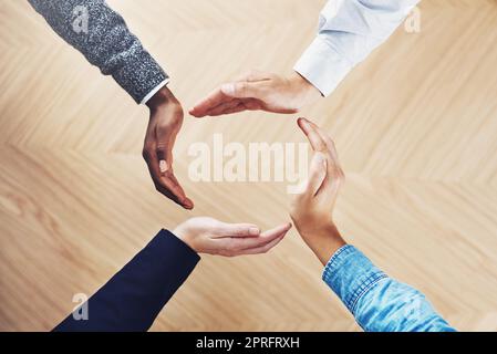 What goes around comes around. High angle shot of a group of unidentifiable businesspeople forming a circle with their hands. Stock Photo