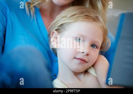 Arent I just the cutest. a mother and her daughter watching something on a tablet while sitting on the sofa at home. Stock Photo