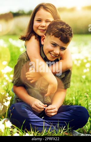 Little sisters can be fun to have around. Portrait of a cute little girl giving her big brother a hug outside. Stock Photo