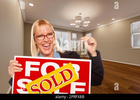 Attractive Young Woman with New Keys and Sold Real Estate Sign In Empty Room of House Stock Photo